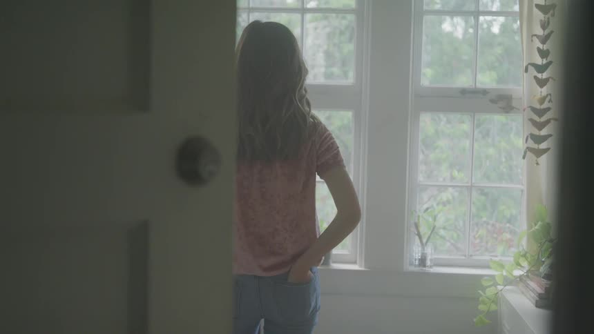 Woman stands in front of a window as she looks outside