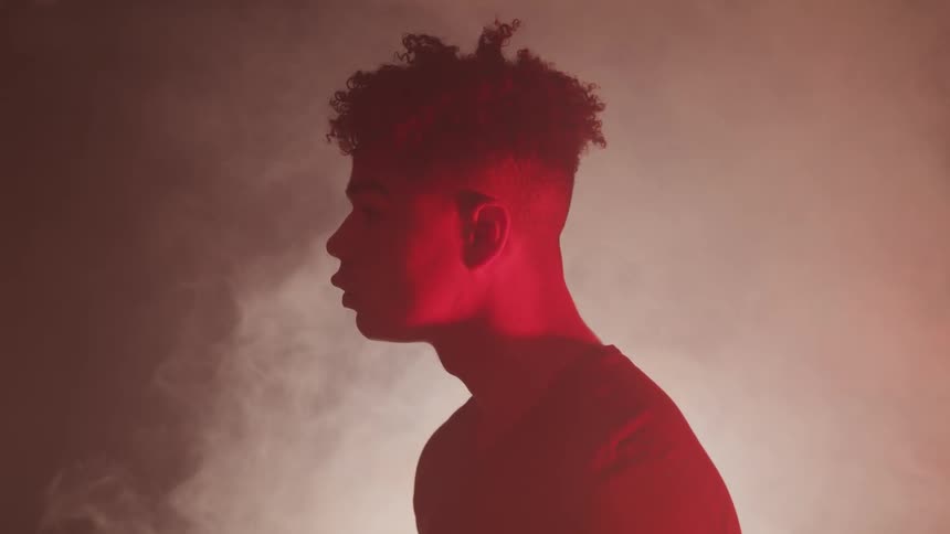 A young black man being illuminated by a red light in a dark and smoky room