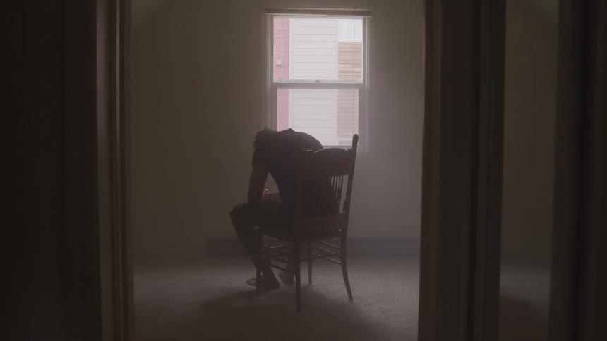 A man sits on a chair with his head bowed