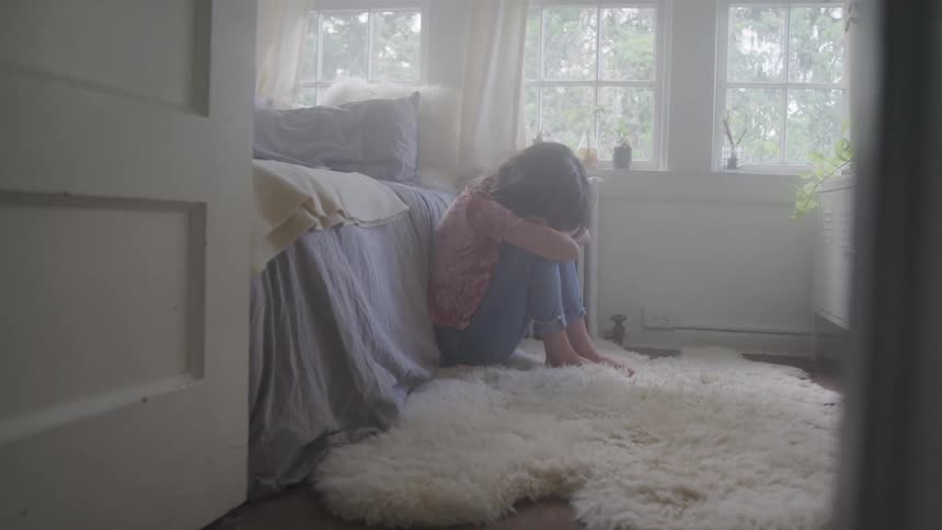Sad female sitting on the floor in her bedroom with her head down