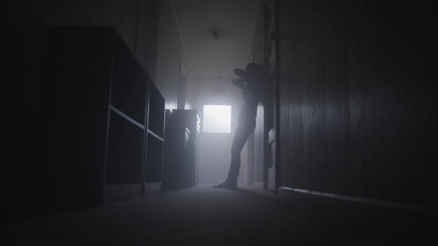 Woman slides down door to sit on floor in dark hallway