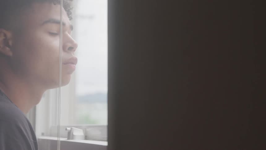 A black teenager looks out the window