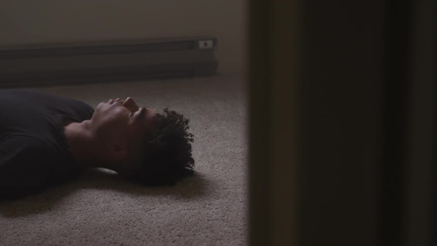 A boy laying in a room on the carpeted floor sleeping near a baseboard heater