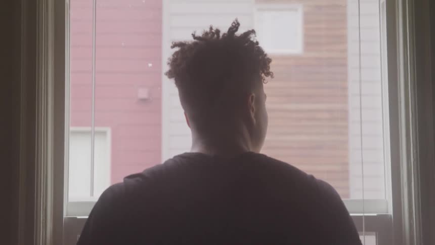 A young black man stares out of a window