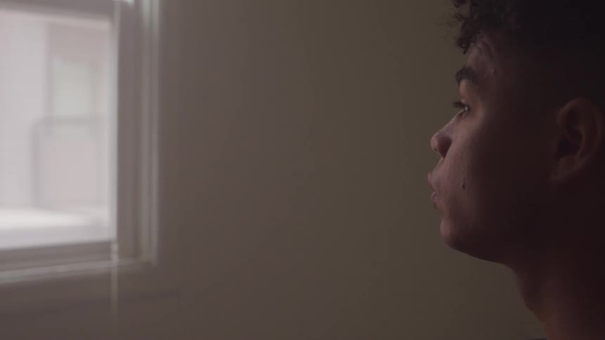 A young man looking out of a window before lowering his head