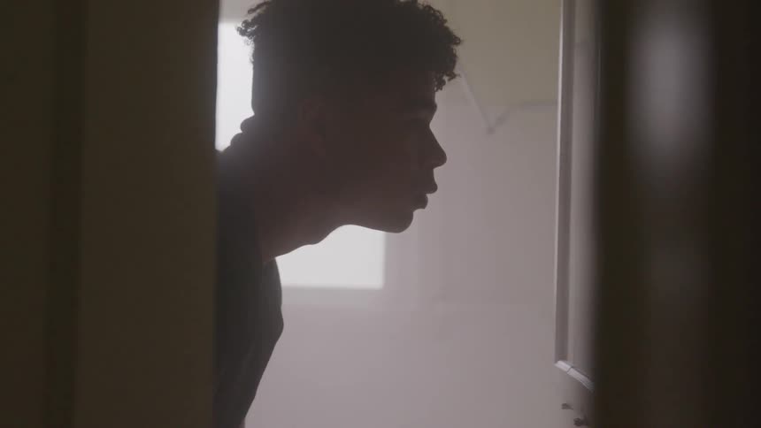 A sad teenager looks in a bathroom mirror