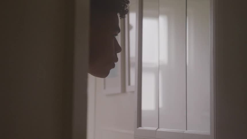 A young black man stands and looks at himself in a mirror