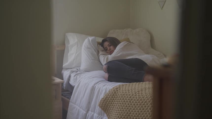 A girl curls up on her bed in a bedroom