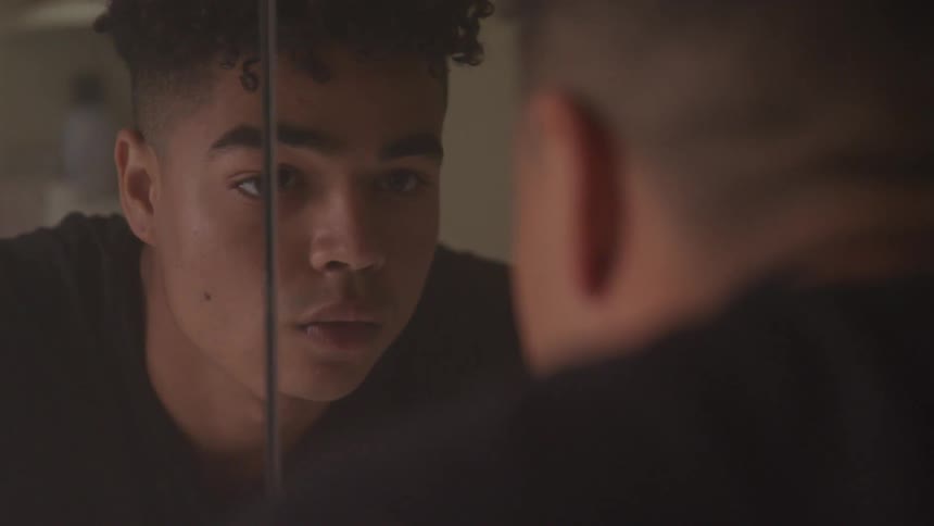 Dark skinned boy looks at himself in the mirror indoors
