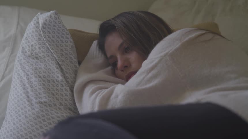 A young woman wearing a white sweater is lying in bed