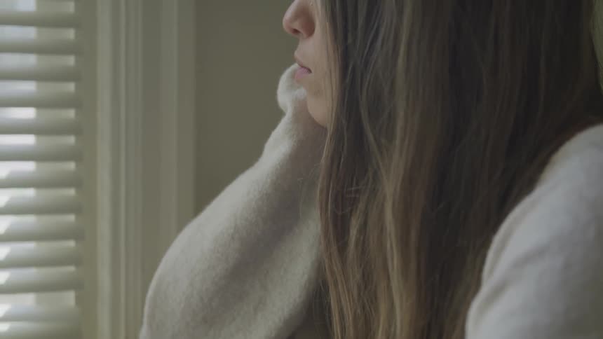 Woman resting her chin on her hands looks out the window at home