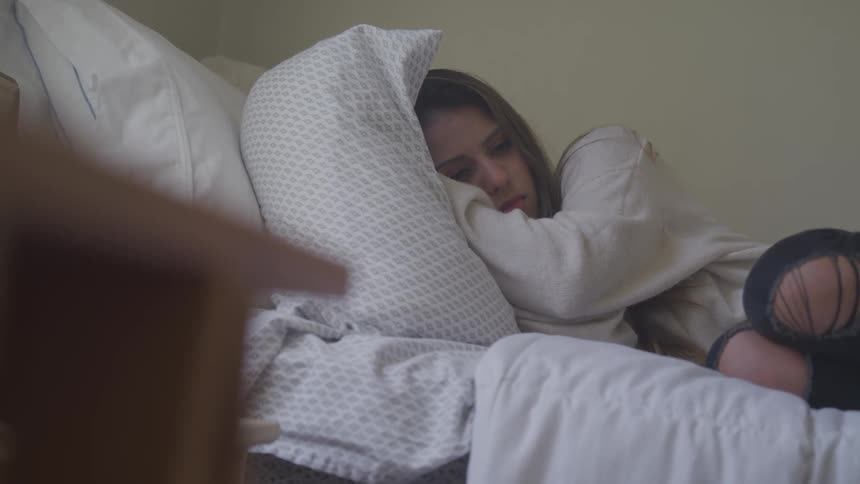 A young woman curled up on a bed with a sad expression on her