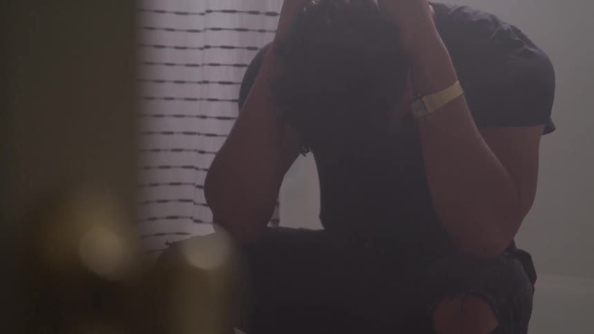 A young black man sits with his head in his hands