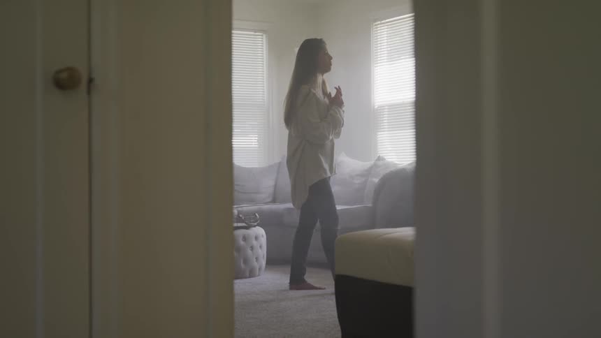 A young female clasps her hands together as she walks through a living room