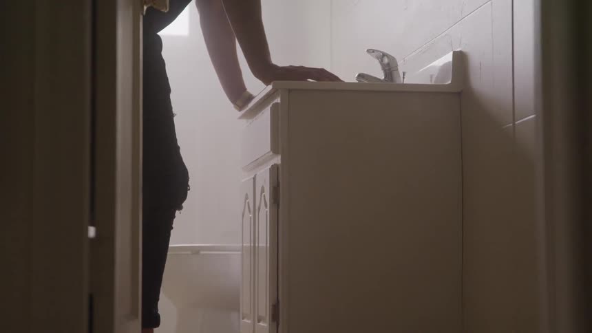 A young man leans up against a bathroom sink
