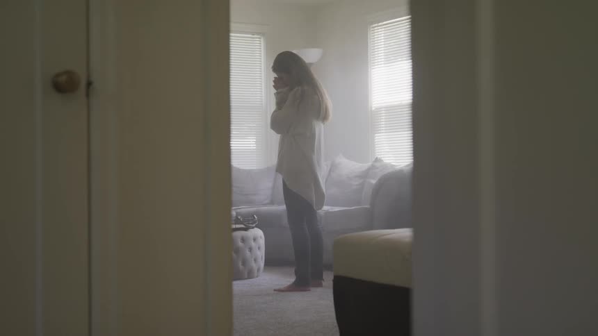 A woman stands in the room with her hands on her face