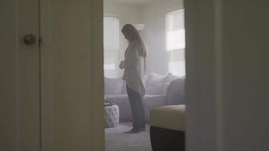 A sad woman stands in a living room