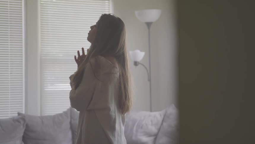 Woman stands in living room looking up and praying