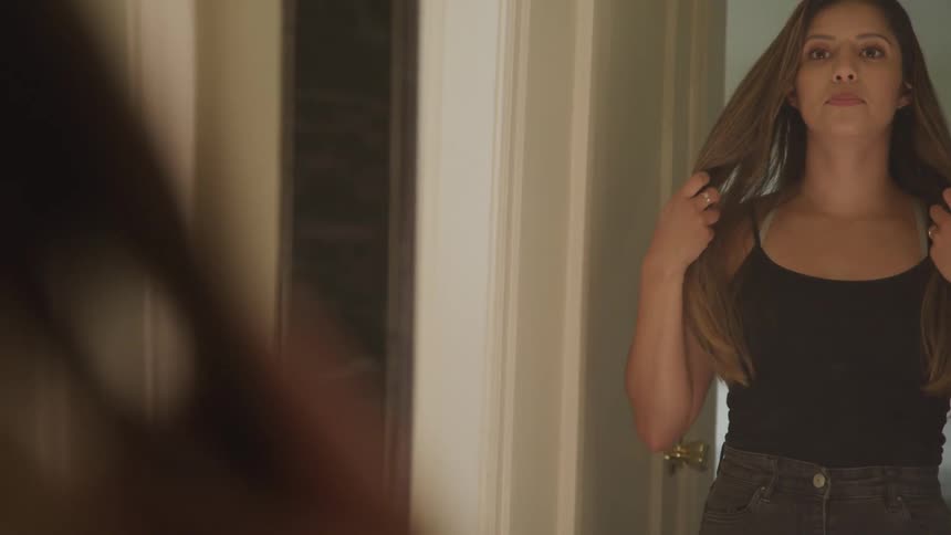A young woman looks in a mirror while fixing her hair