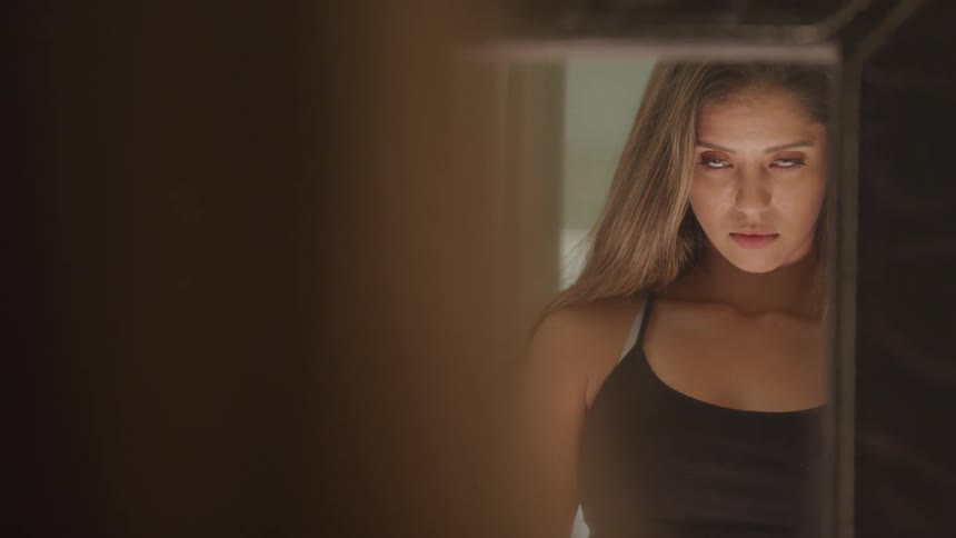 A woman lifts her head and looks at her reflection in a mirror