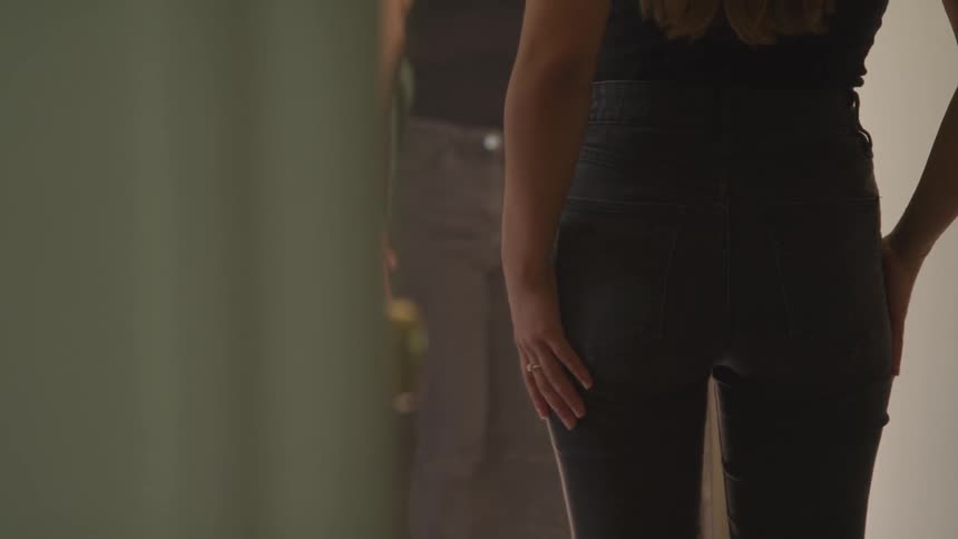 A young woman in tight jeans runs her hand over her rear end