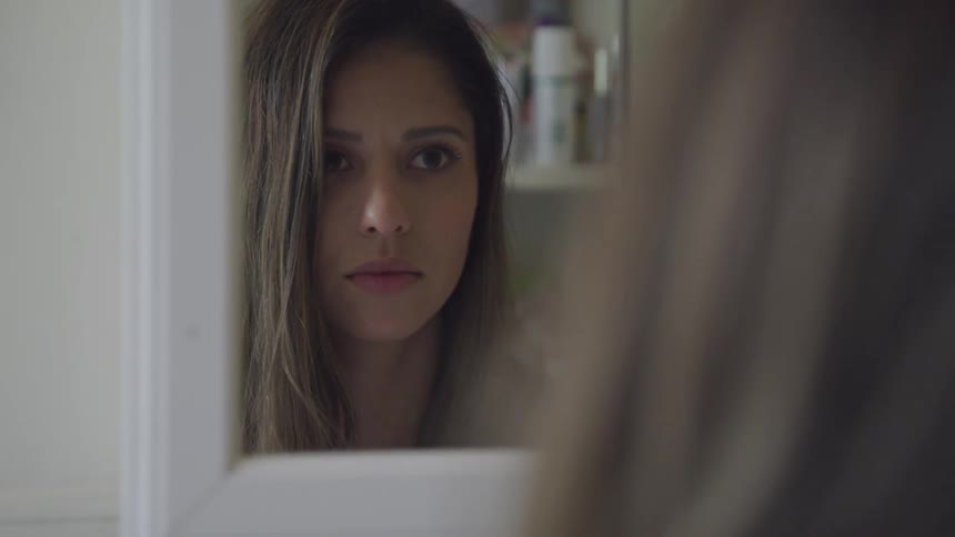 A woman looks into a mirror and then looks down