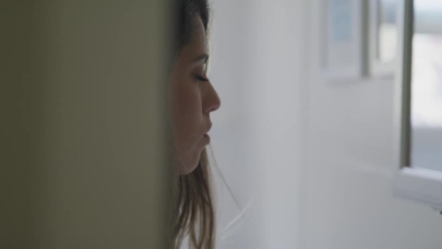 A woman lifts her head and looks into the mirror over the bathroom sink