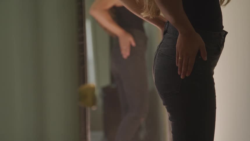 A woman checks her outfit in a full length mirror