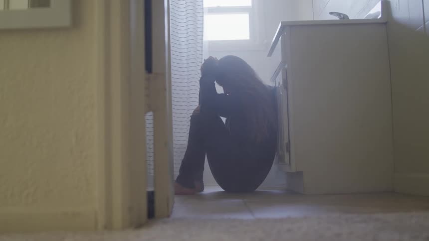 A woman sits on the bathroom floor by a sink