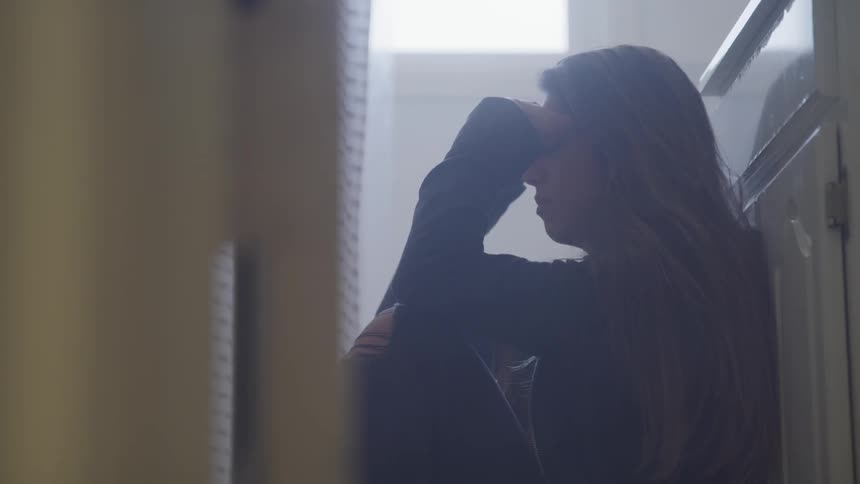 A stressed young woman sitting on the floor leaning against a cabinet