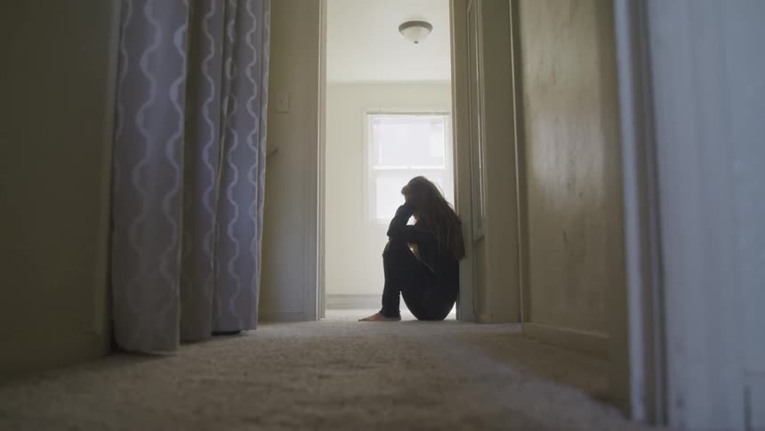 A young female is distraught as she rests her back against a door frame and sinks to the ground