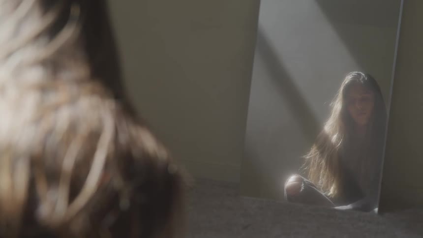 Woman sitting on the floor of a room looking at her reflection on a mirror
