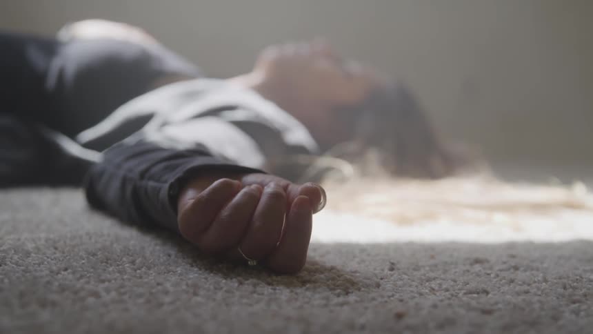 A young female lays on her back on a carpeted floor indoors as sunlight shines on her through a window