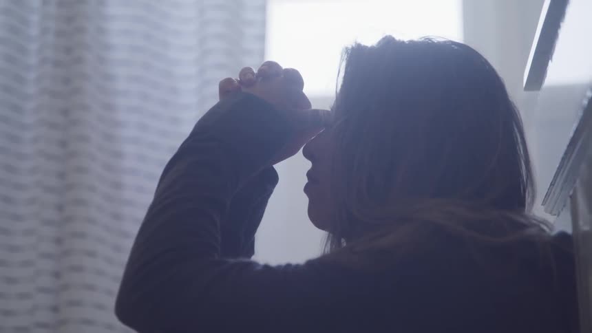 A young woman sits in a bathroom and puts her face in her hands