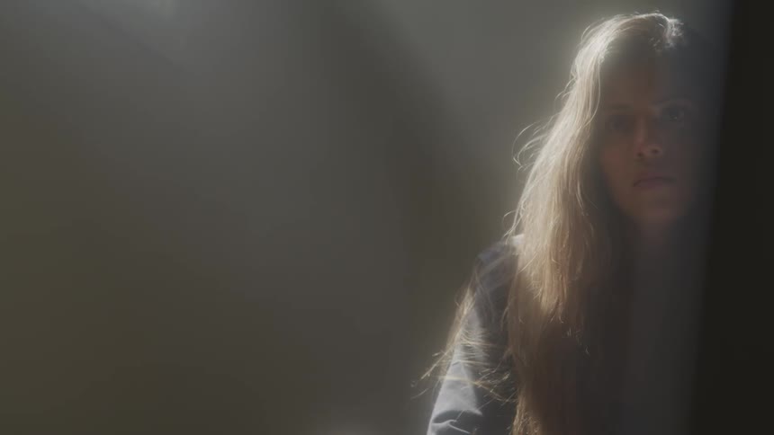 A female looks up from the floor as she stands under a light source