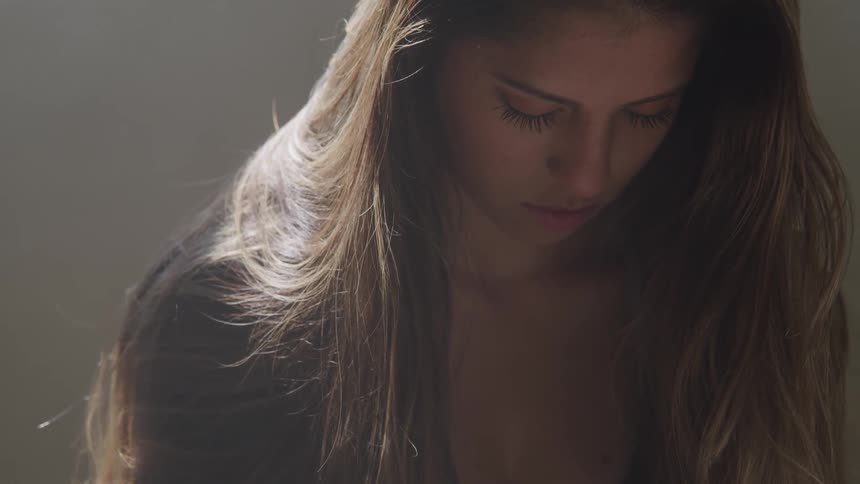 A young woman sits still in a room while looking downward as she is concentrating