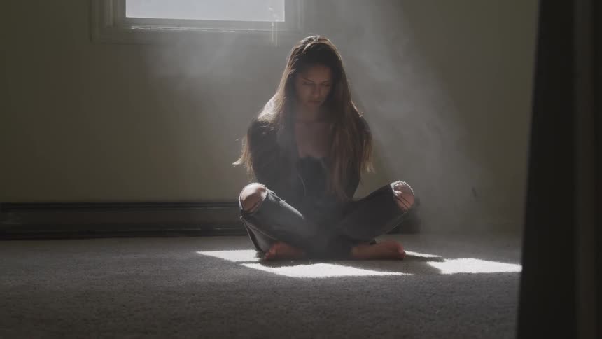 Woman sits cross legged in sunshine shining through window