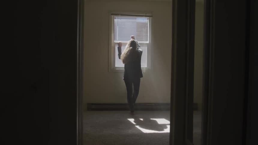 A young girl stands and looks out the window