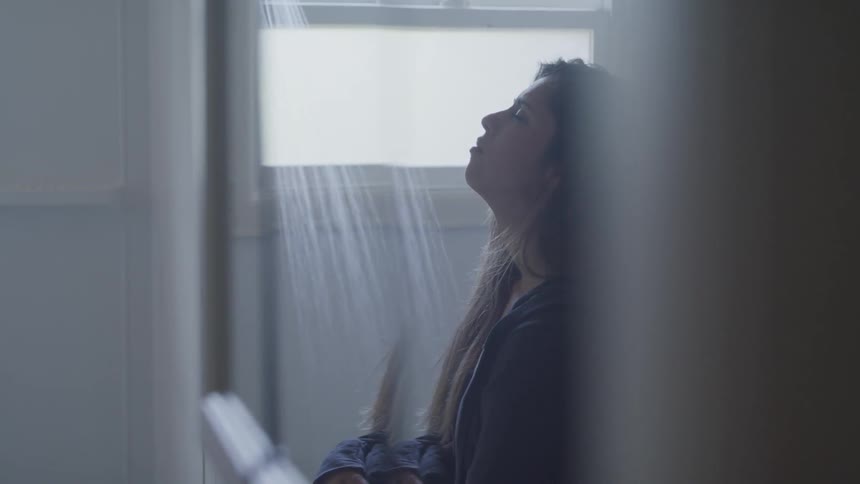 A woman stands in a bathroom with the shower running