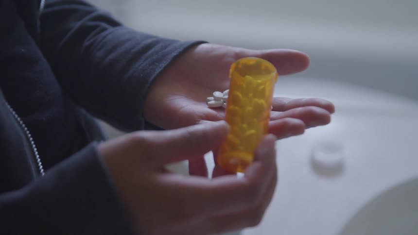 A person pouring white pills into their hand