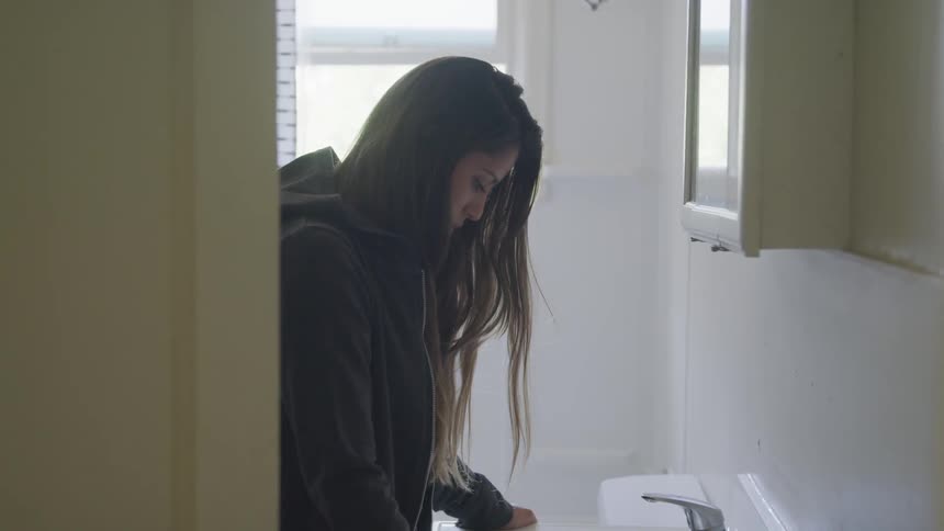 A woman stands against a sink in a bathroom