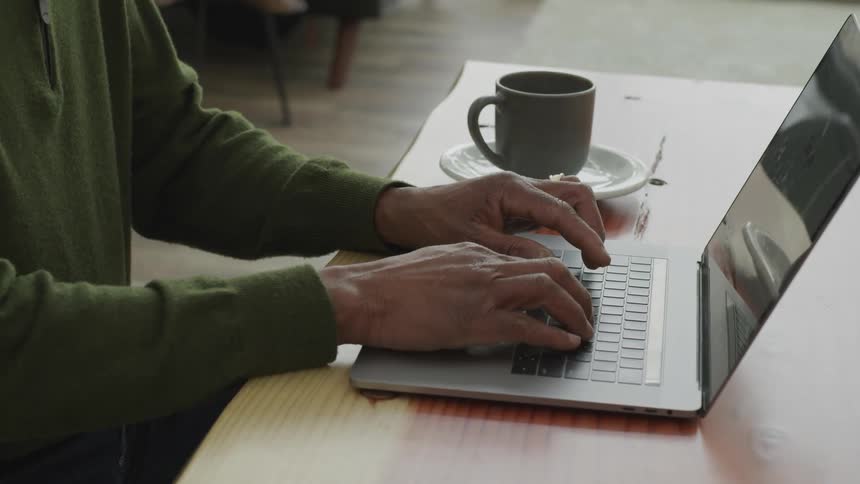 A man types on a laptop next to a cup of coffee