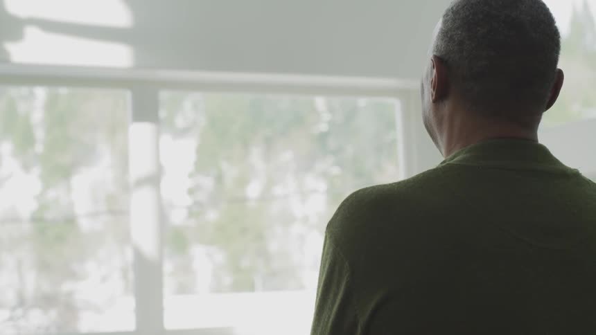 A man is standing in his home looking at the window