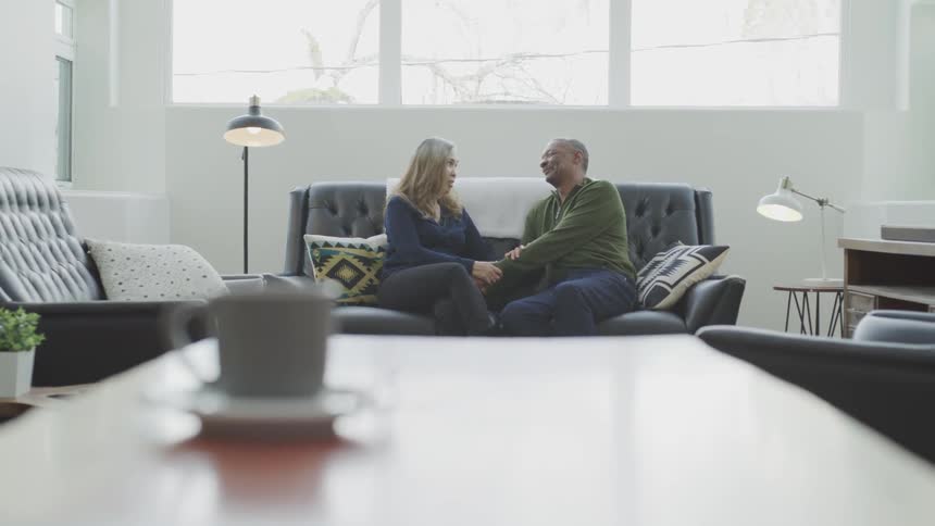 A man and woman sit on a couch and hold hands and talk