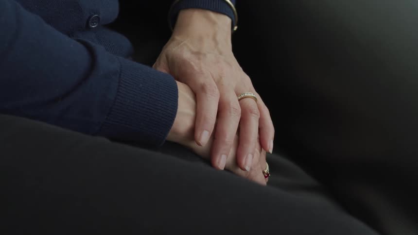 A woman sits with her hands clasped in her lap