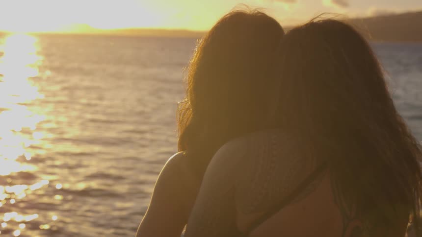 Two people hug by the shore at sunset