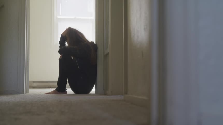 A woman leaned up against a doorway and then sits down on the floor