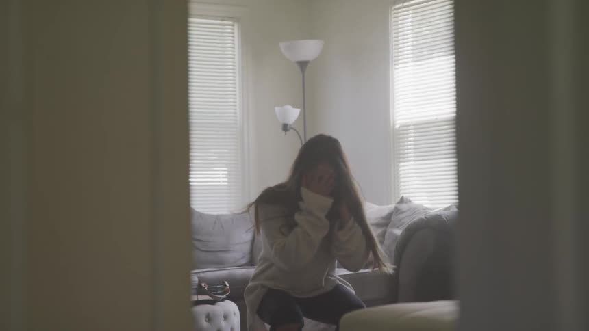 A young woman is standing with her head in her hands and falls to her knees