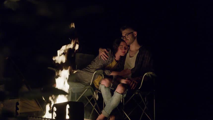 A couple sit together by the campfire at night