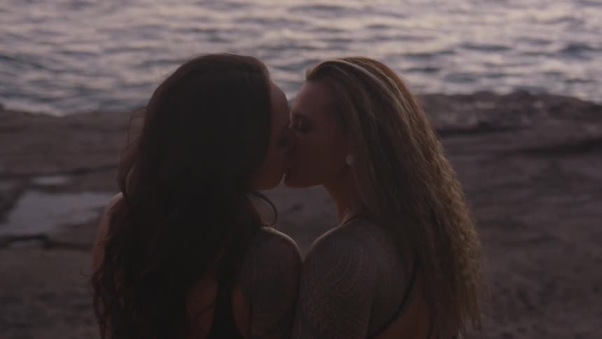 Two women kiss on the beach at sunset